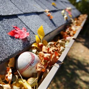 clogged gutters example. Fall leaves and a baseball are stuck in a residential home's gutter system