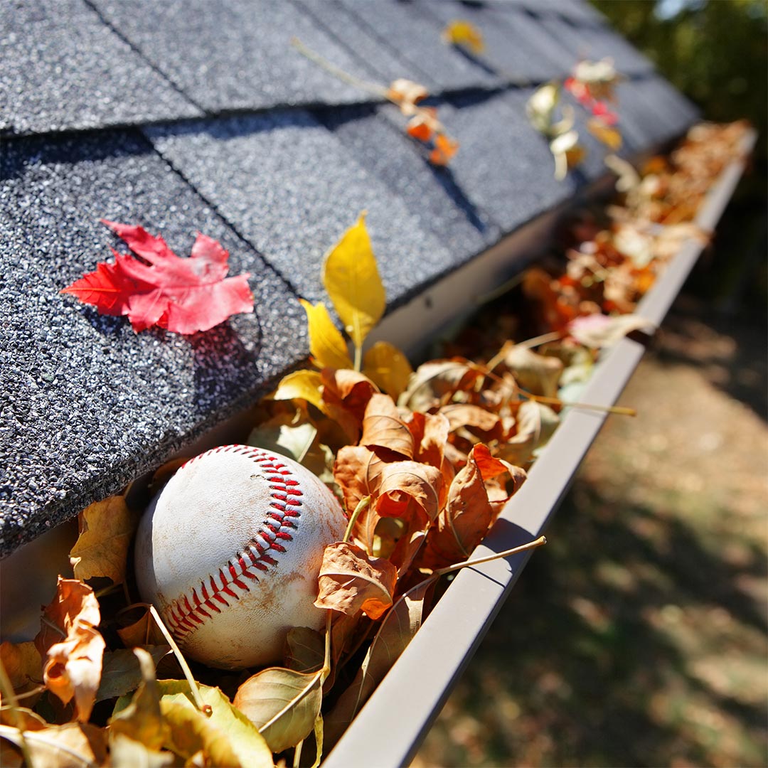 clogged gutters example. Fall leaves and a baseball are stuck in a residential home's gutter system