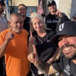 Vertical Roofing Co team members and homeowners pose together outside after a completed roofing-related visit, smiling and holding up one finger.