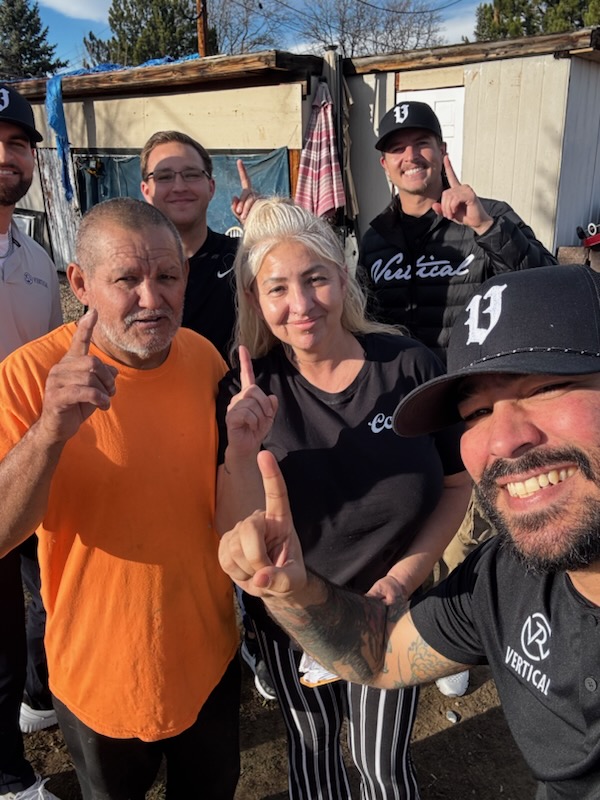 Vertical Roofing Co team members and homeowners pose together outside after a completed roofing-related visit, smiling and holding up one finger.