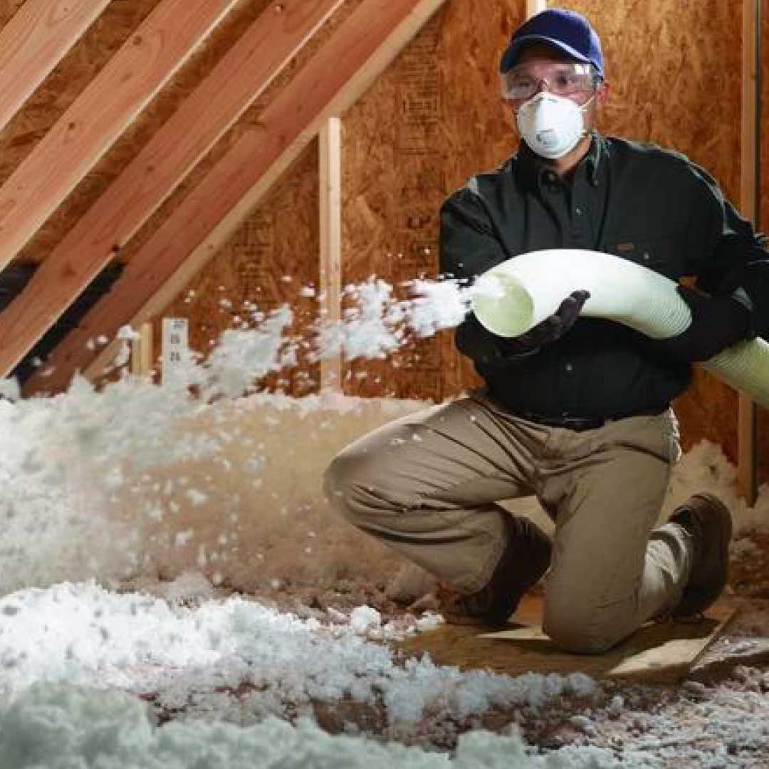 Contractor kneeling in an attic with blown-in insulation.