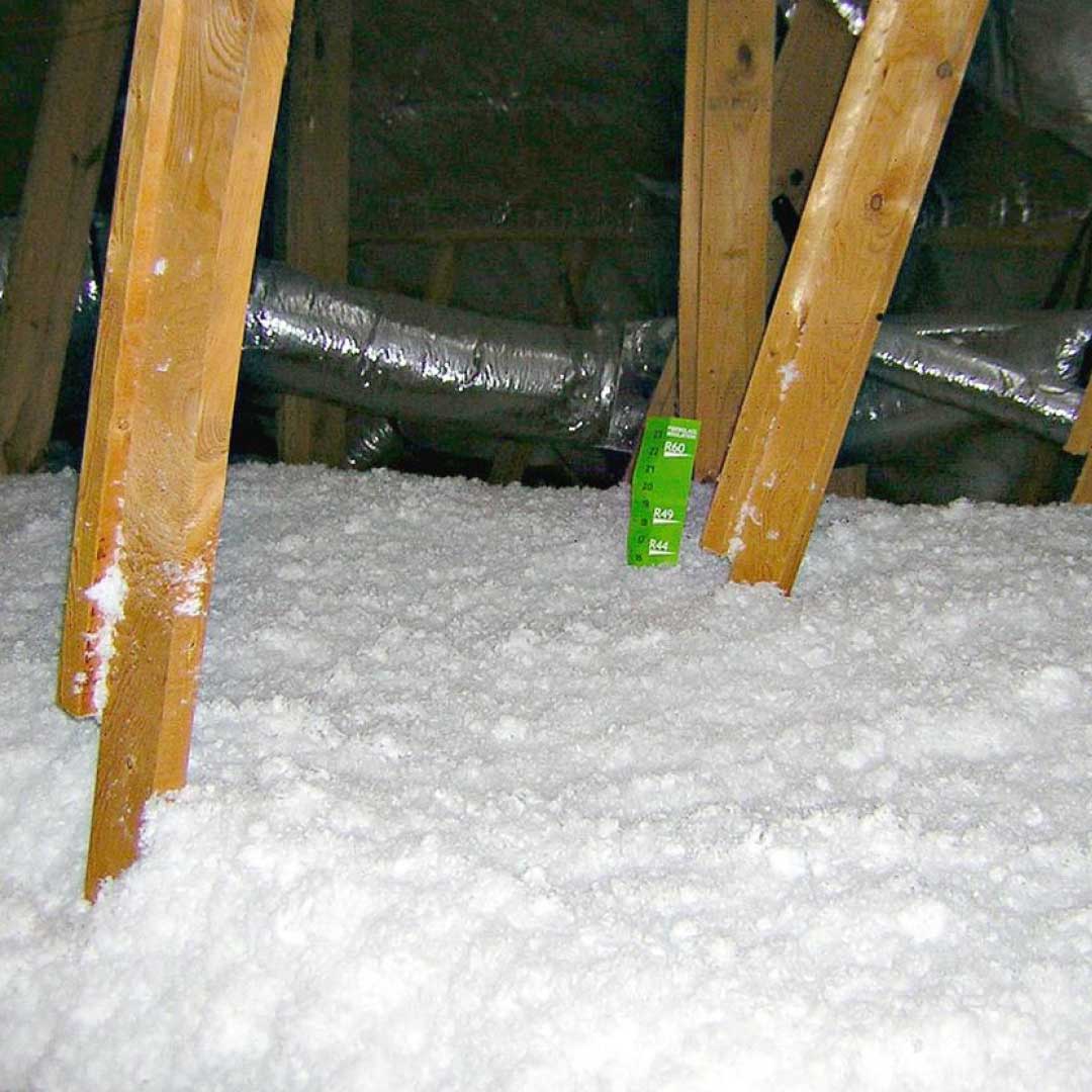 Attic space with blown-in insulation around wood framing.